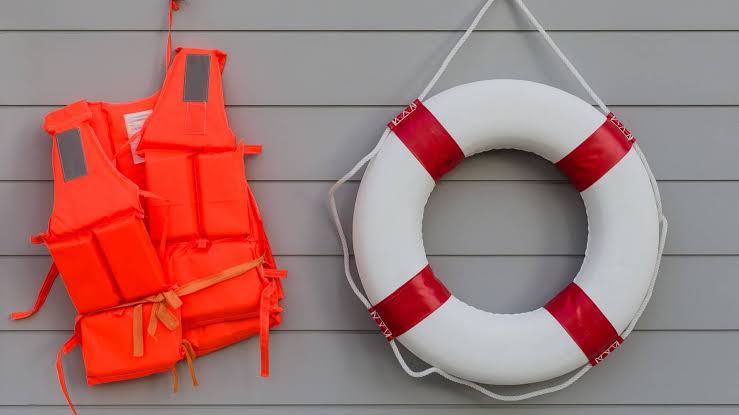 Orange life vests and a white life ring hanging on a grey wall